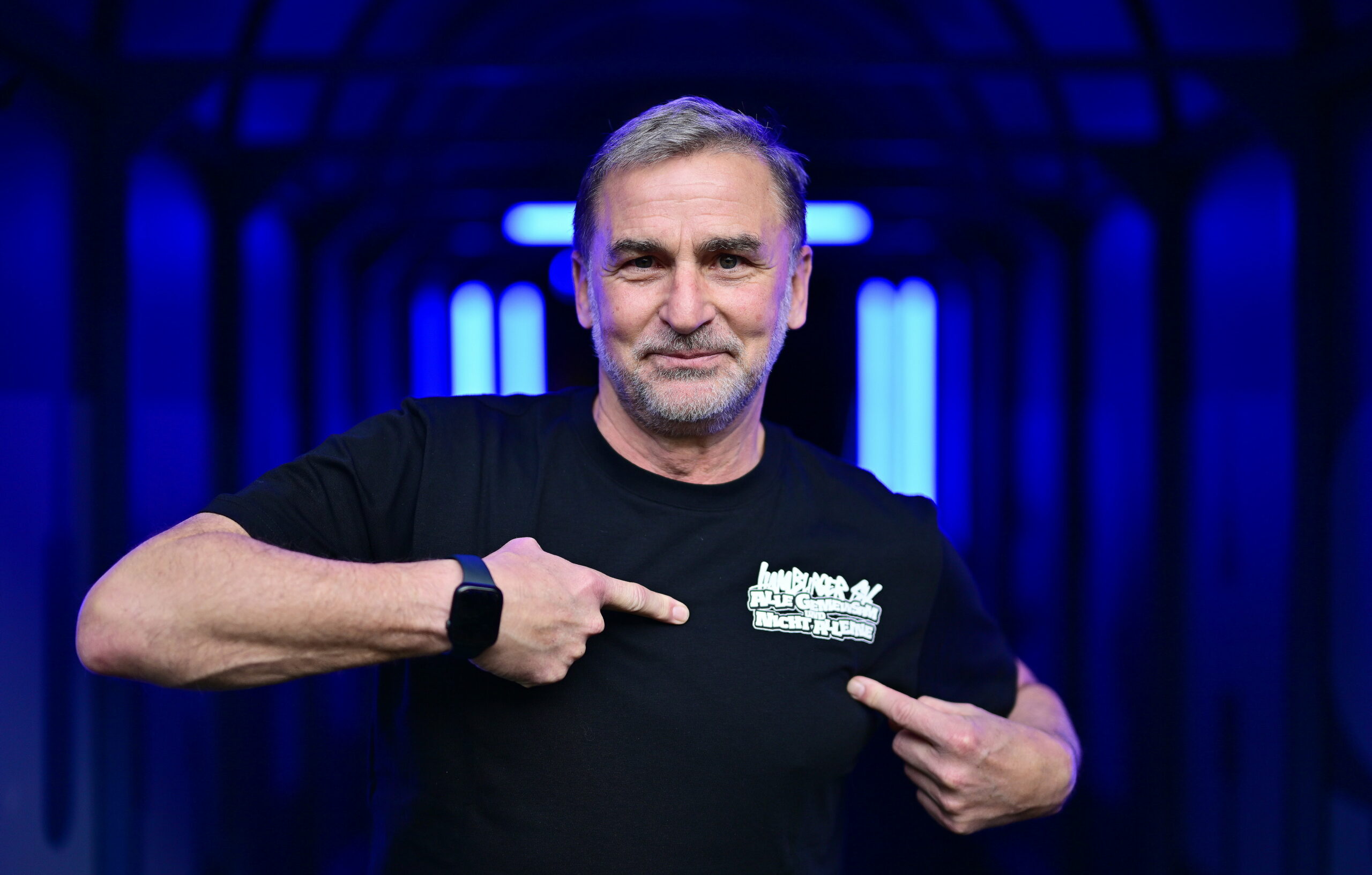 Stefan Kuntz zeigt auf sein HSV-Shirt