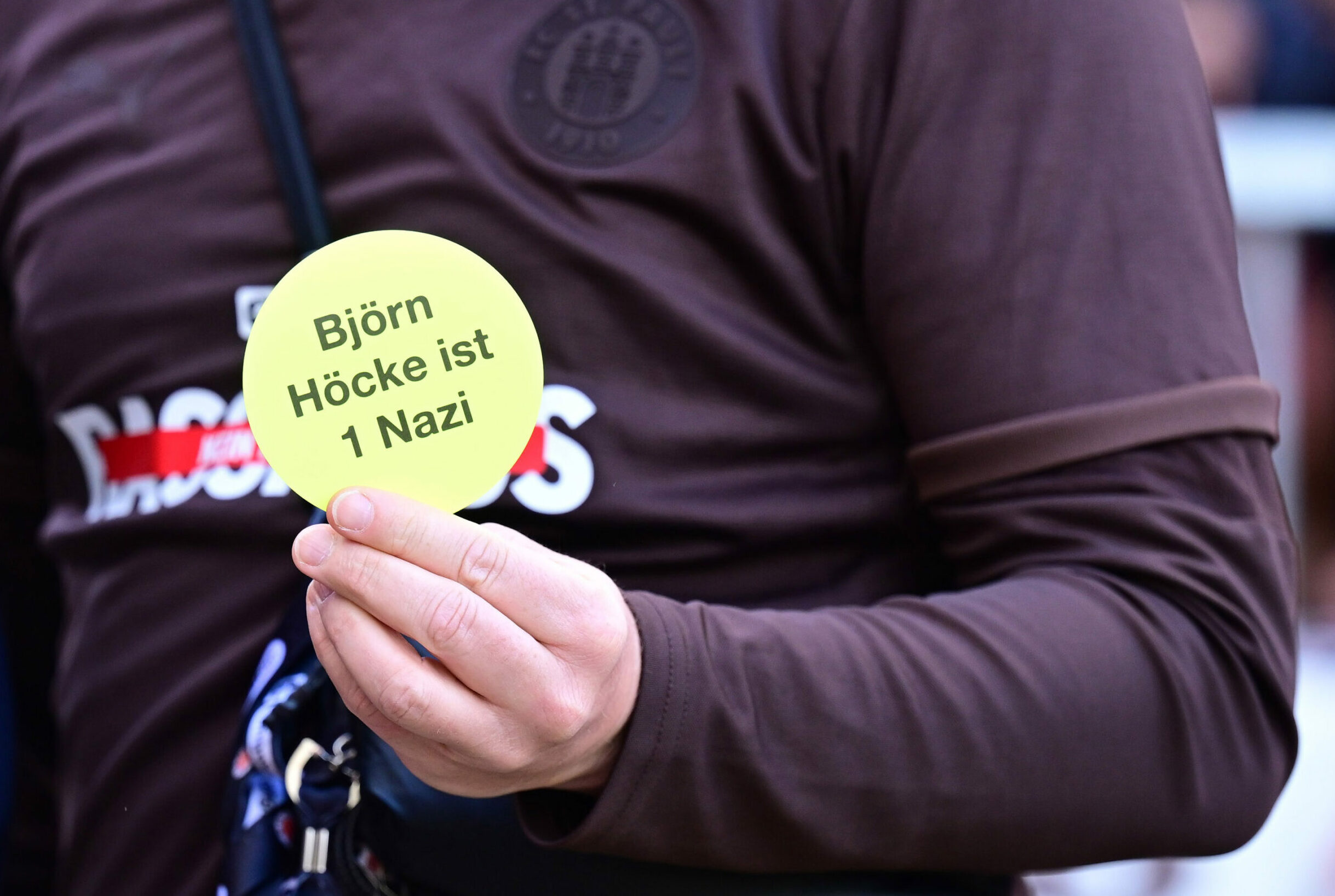 Vor dem Spiel gegen Stuttgart hielt St. Pauli-Präsident Oke Göttlich einen Anti-AfD-Sticker in die Kameras.