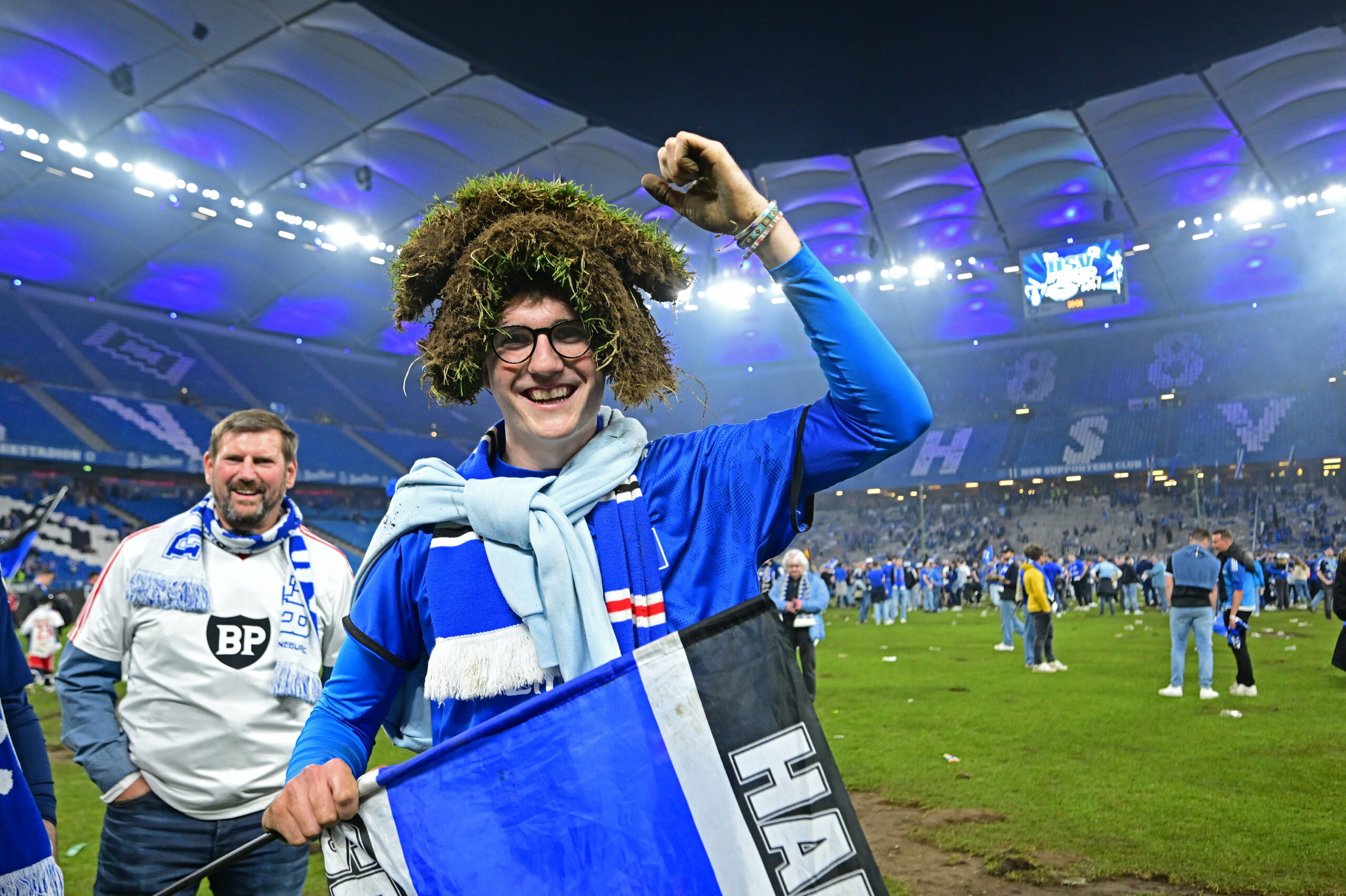 Ein HSV-Fan lächelt mit einem Stück Rasen auf dem Kopf im Volksparkstadion
