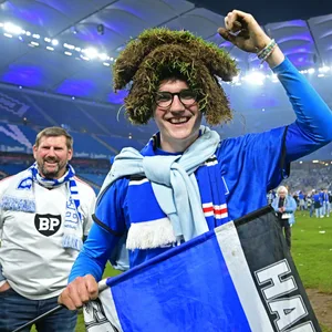 Ein HSV-Fan lächelt mit einem Stück Rasen auf dem Kopf im Volksparkstadion