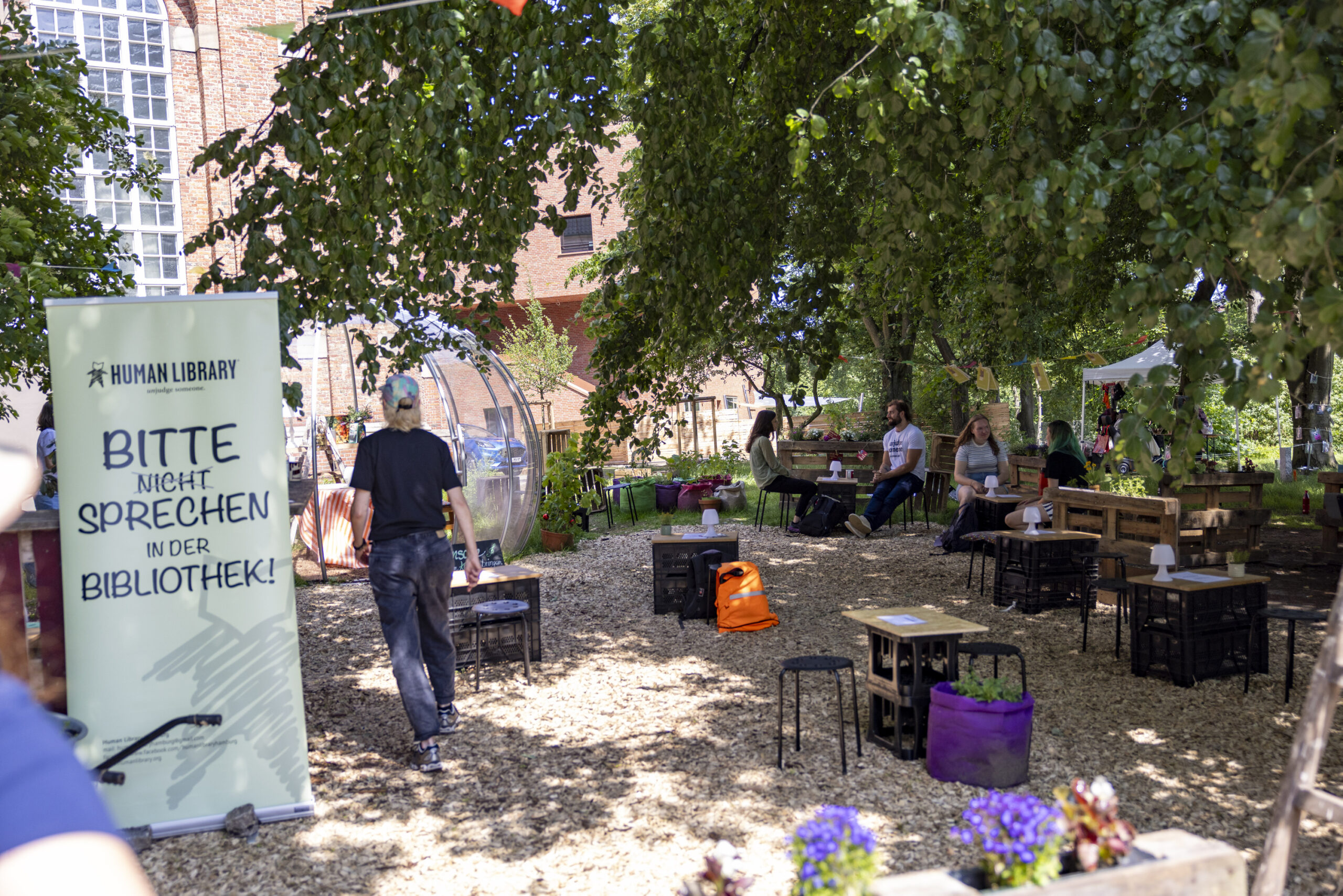 Die Human Library Hamburg bei der Eröffnung des Trinitatis Quartiers in Altona. Viele kleine Tische und Stühle, auf denen Menschen sitzen.