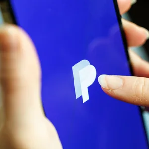 Eine Frau hält ein Smartphone mit der Paypal-App in der Hand.