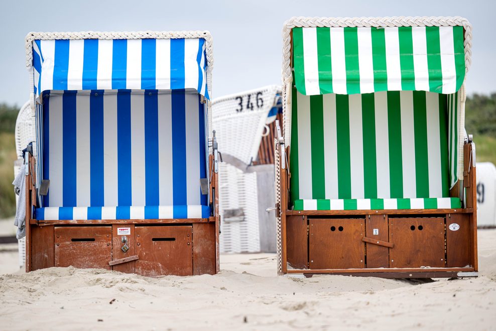Ein blauer und ein grüner Strandkorb stehen nebeneinander.