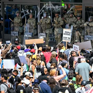 Menschen protestieren in Los Angeles während Einsatzkräfte der Nationalgarde vor einem Regierungsgebäude stehen.