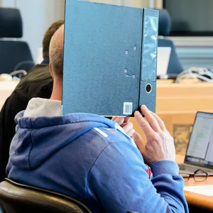 Der Angeklagte verdeckt sich mit einem Ordner das Gesicht.