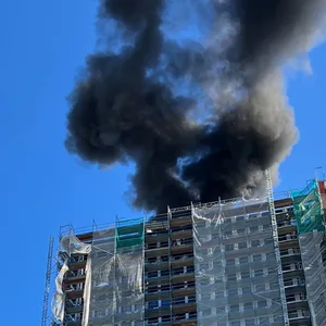 Schwarzer Rauch steigt vor blauem Himmel aus einem Hochhaus empor