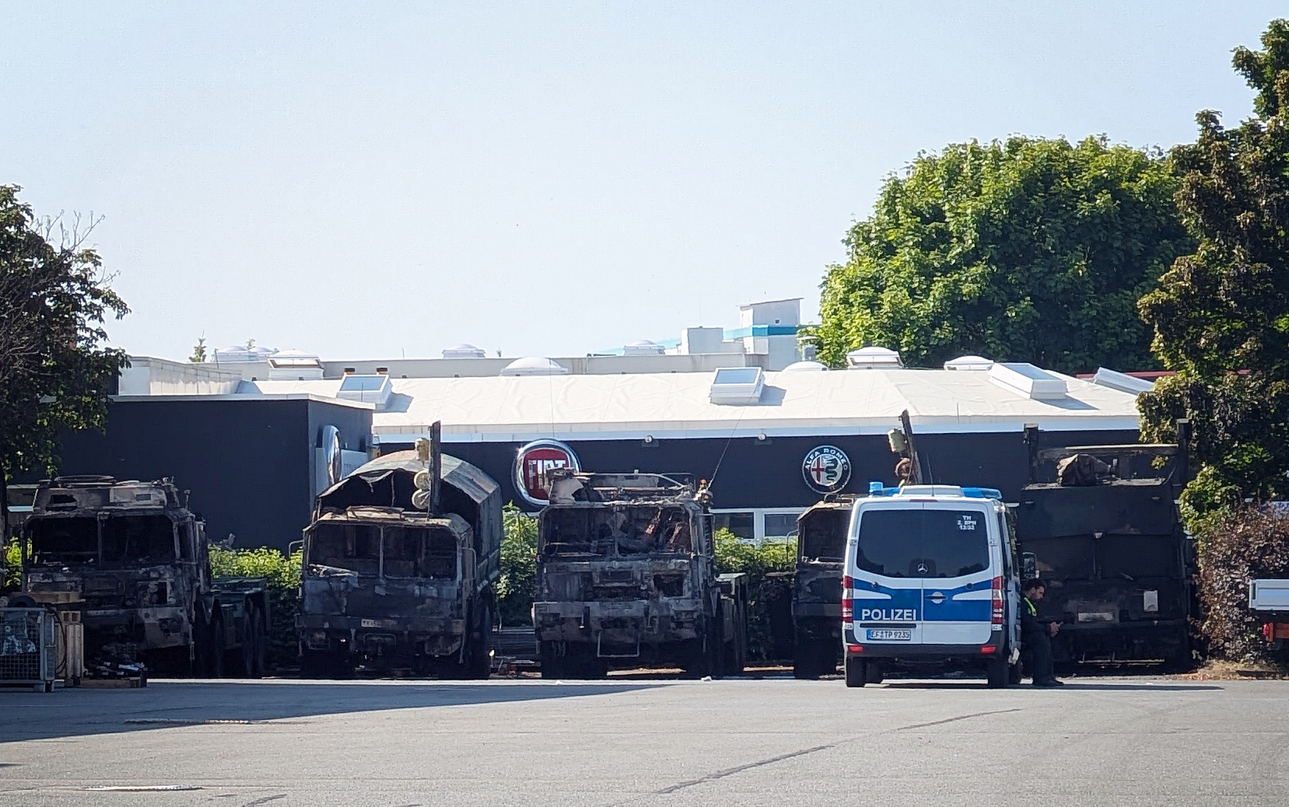 Ein Polizeifahrzeug steht vor mehreren verbrannten Militärlastern auf dem Gelände eines Nutzfahrzeug-Serviceunternehmen.