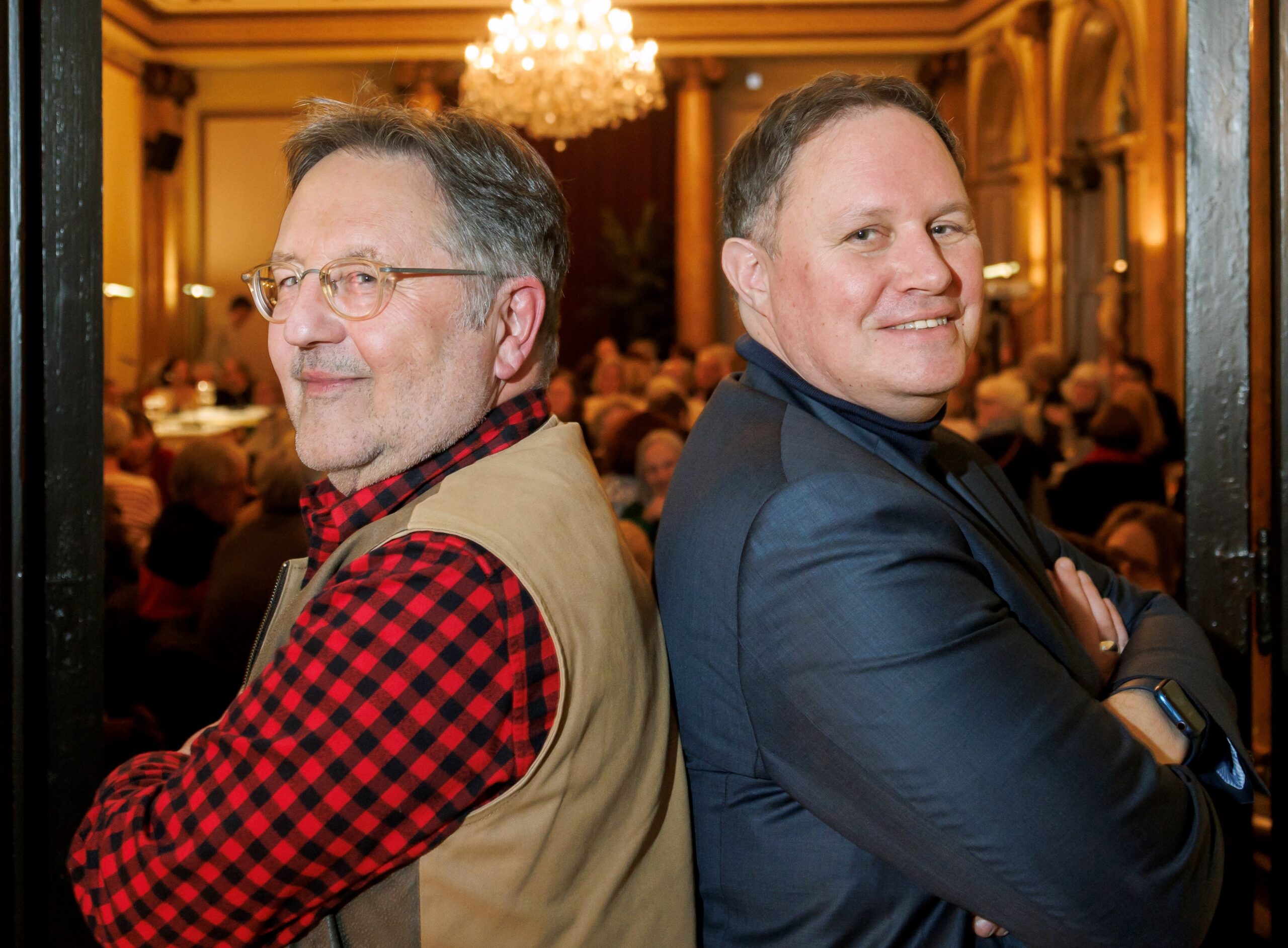Links Moritz, rechts Brosda, sie stehen Rücken an Rücken und schauen in die Kamera. Im Hintergrund Publikum im Literaturhaus