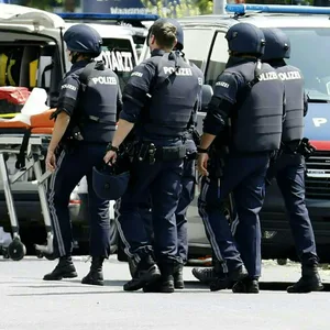Einsatzkräfte der Polizei stehen in der Nähe des Tatorts an einer Grazer Schule.