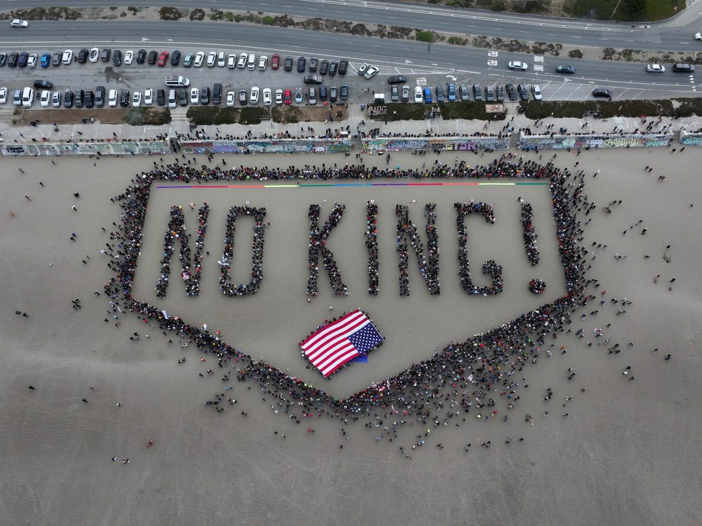 Menschen bilden die Wörter „No King!“ auf einem Strand.