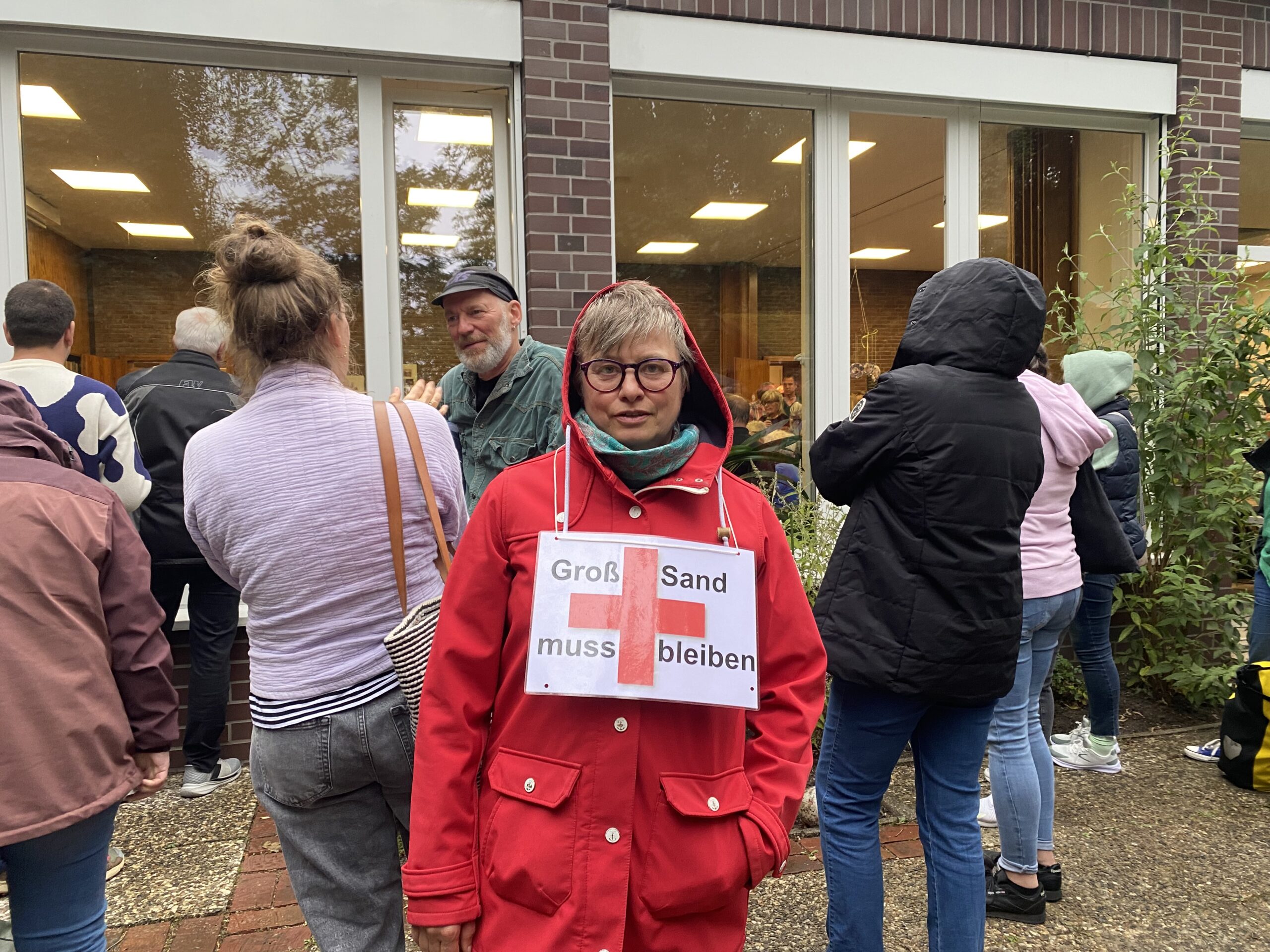 Eine Wilhelmsburgerin hat ein Schild um den Hals hängen. Darauf steht: „Groß-Sand muss bleiben.“