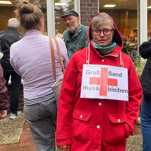 Eine Wilhelmsburgerin hat ein Schild um den Hals hängen. Darauf steht: „Groß-Sand muss bleiben.“
