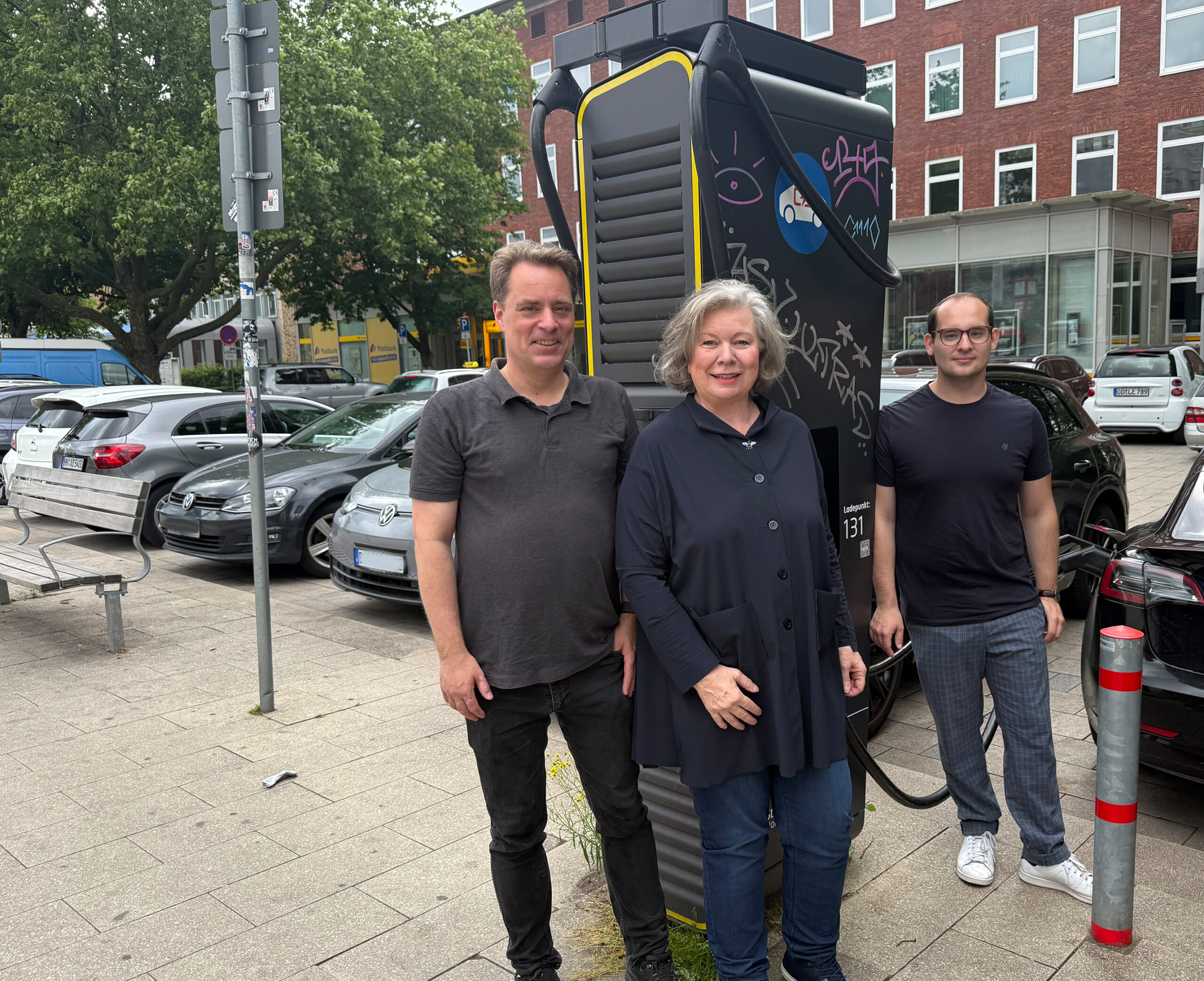 Zwei Männer und eine Frau stehen vor einer E-Ladesäule.