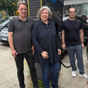 Zwei Männer und eine Frau stehen vor einer E-Ladesäule.