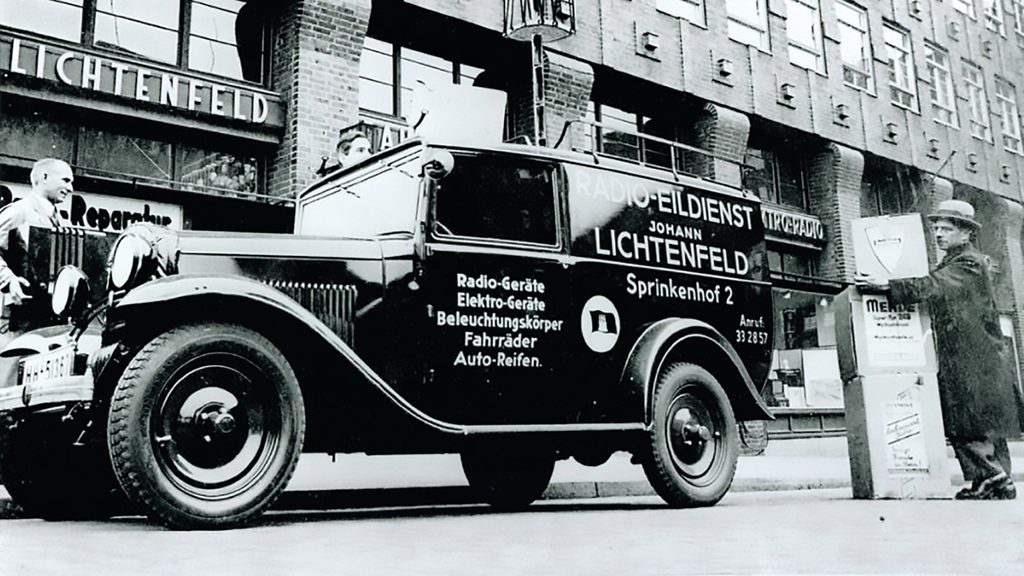 Schwarz-weiß Bild: Auto mit der Aufschrift „Radio-Eildienst Johann Lichtenfeld“ steht vor dem damaligen Laden „Lichtenfeld“