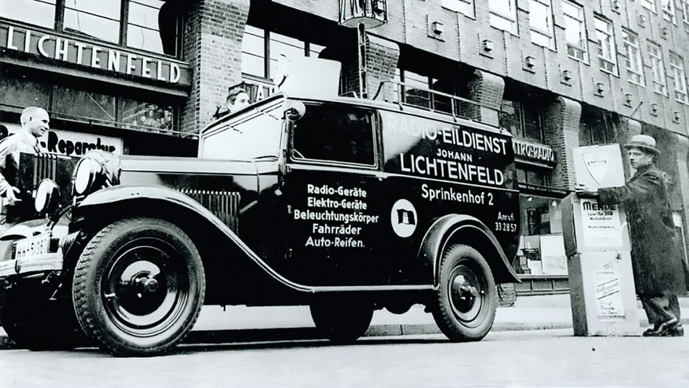 Schwarz-weiß Bild: Auto mit der Aufschrift „Radio-Eildienst Johann Lichtenfeld“ steht vor dem damaligen Laden „Lichtenfeld“