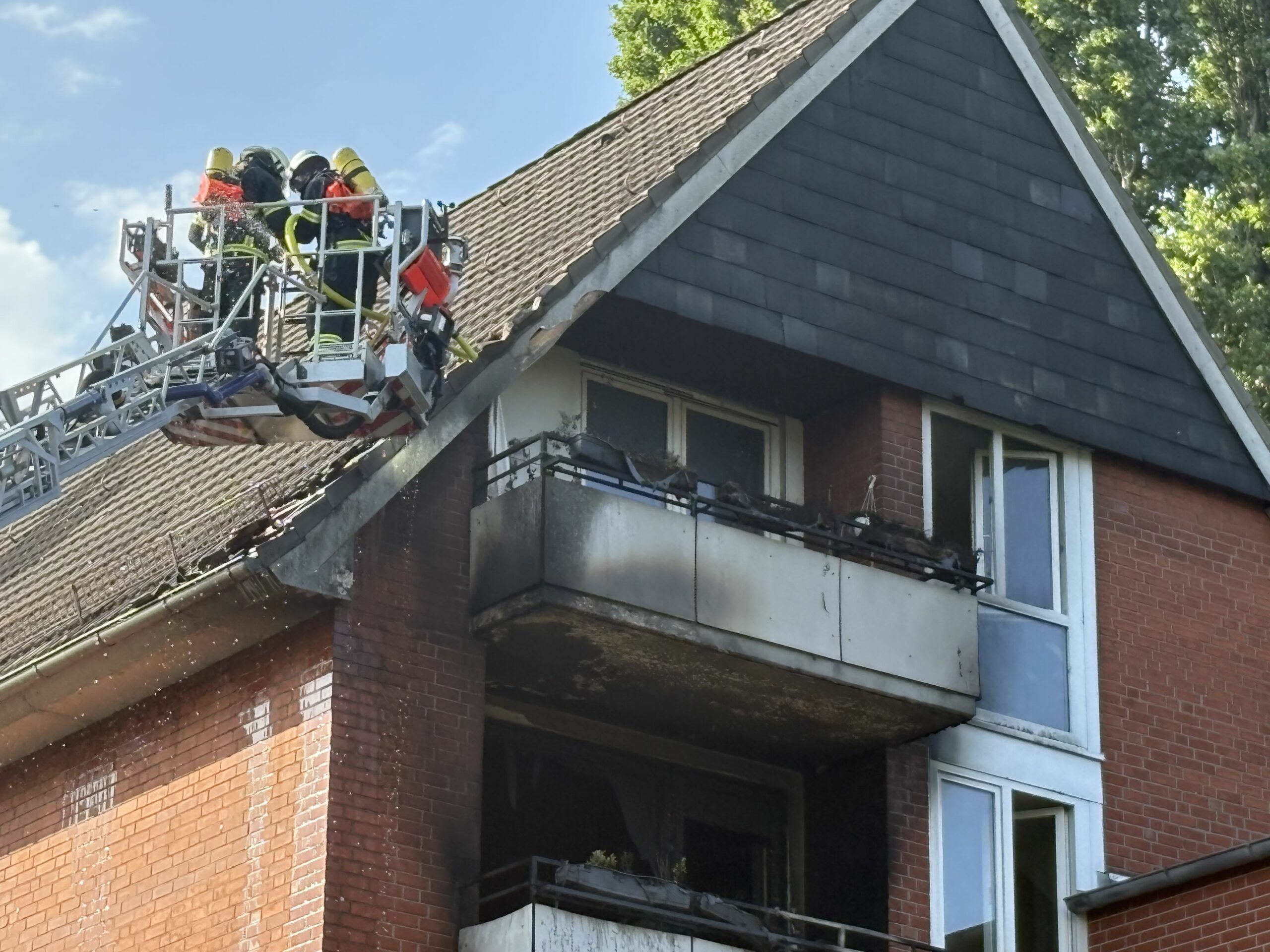 Feuerwehrleute begutachten von einer Drehleiter aus das vom Brand betroffene Dach.