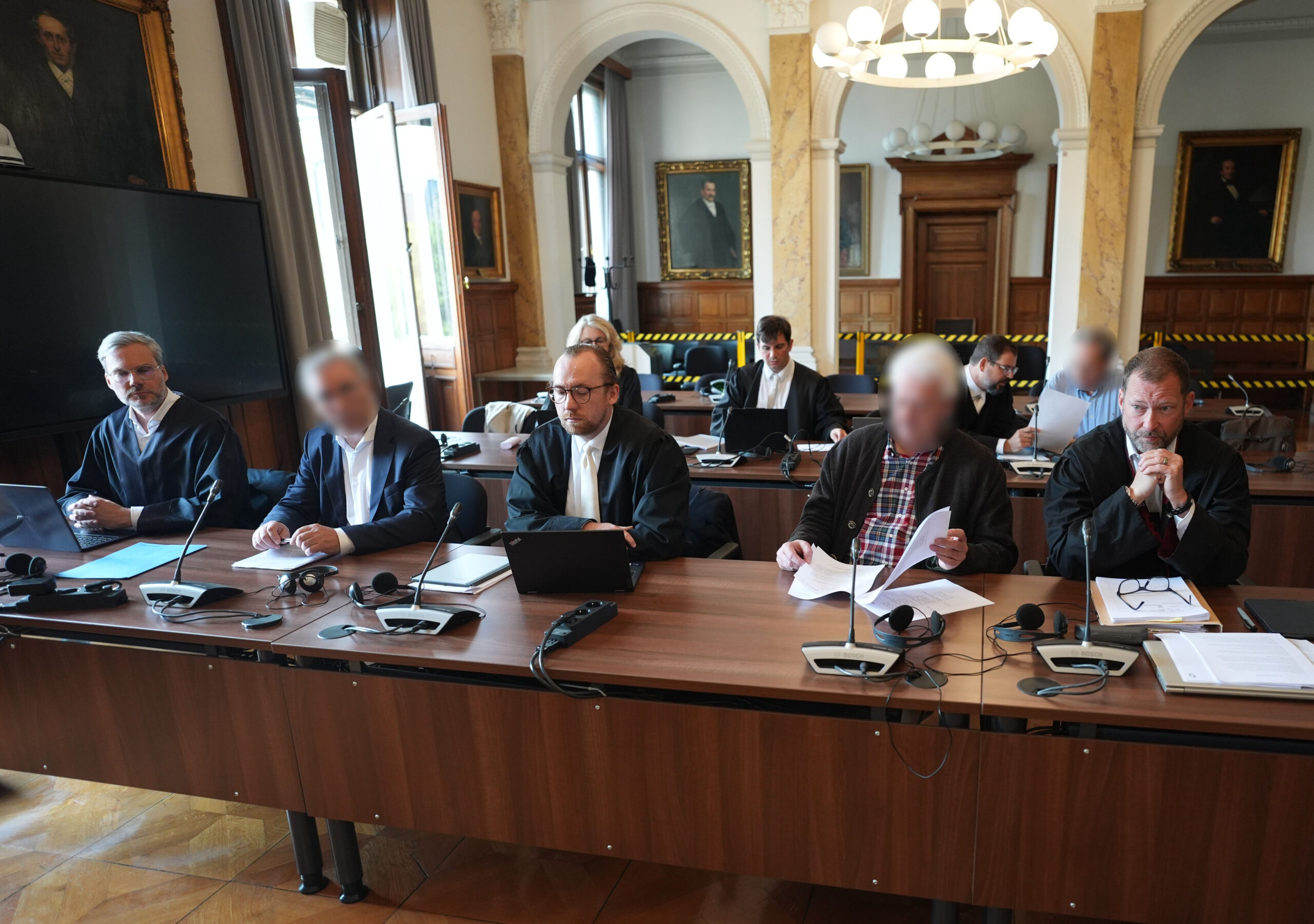 Die drei Angeklagten (vorn 2.v.l., vorn 2.v.r. sowie hinten r.) sitzen neben ihren Anwälten im Ziviljustizgebäude in Hamburg.