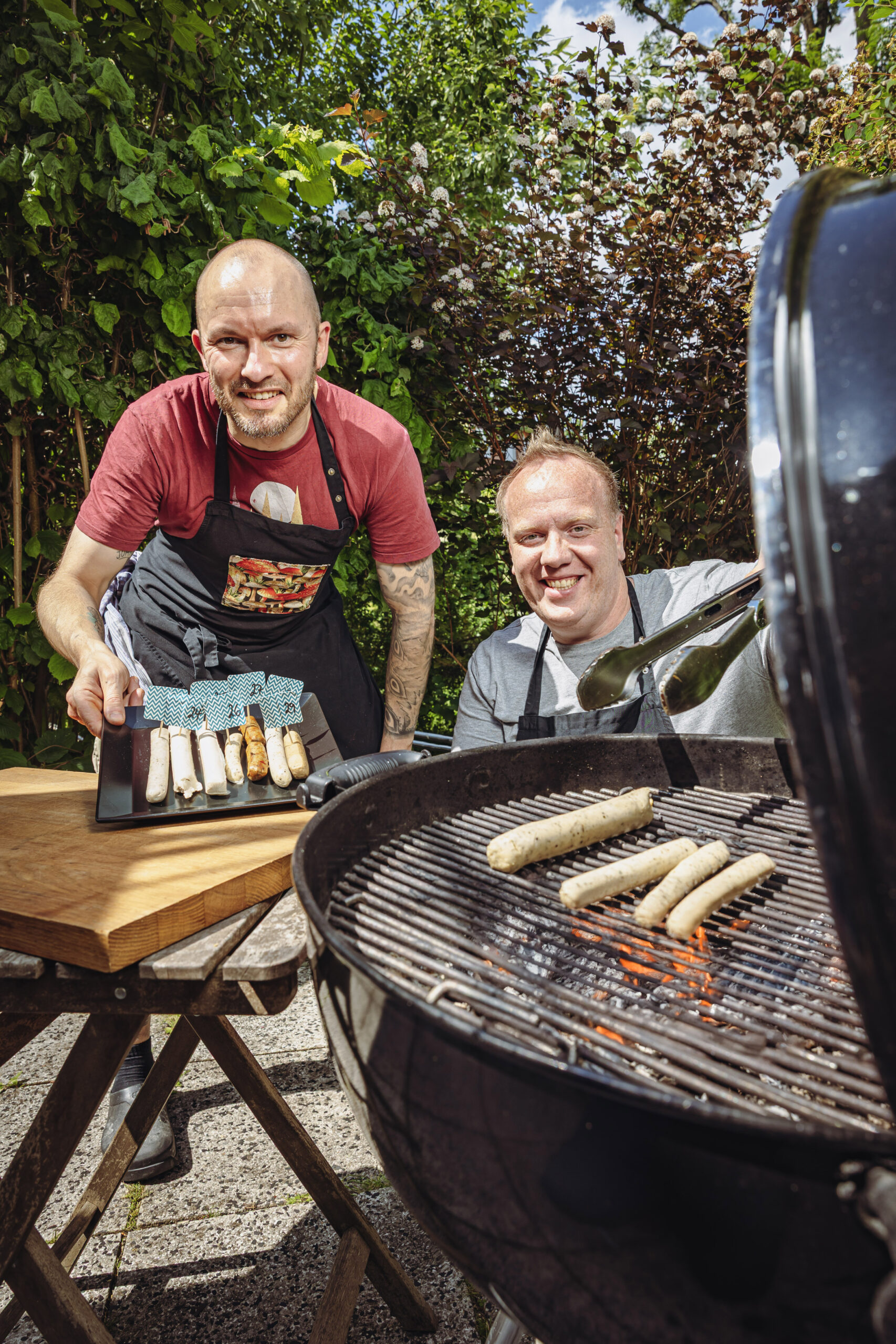 Zwei Männer grillen Bratwürste.