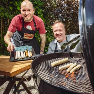 Zwei Männer grillen Bratwürste.