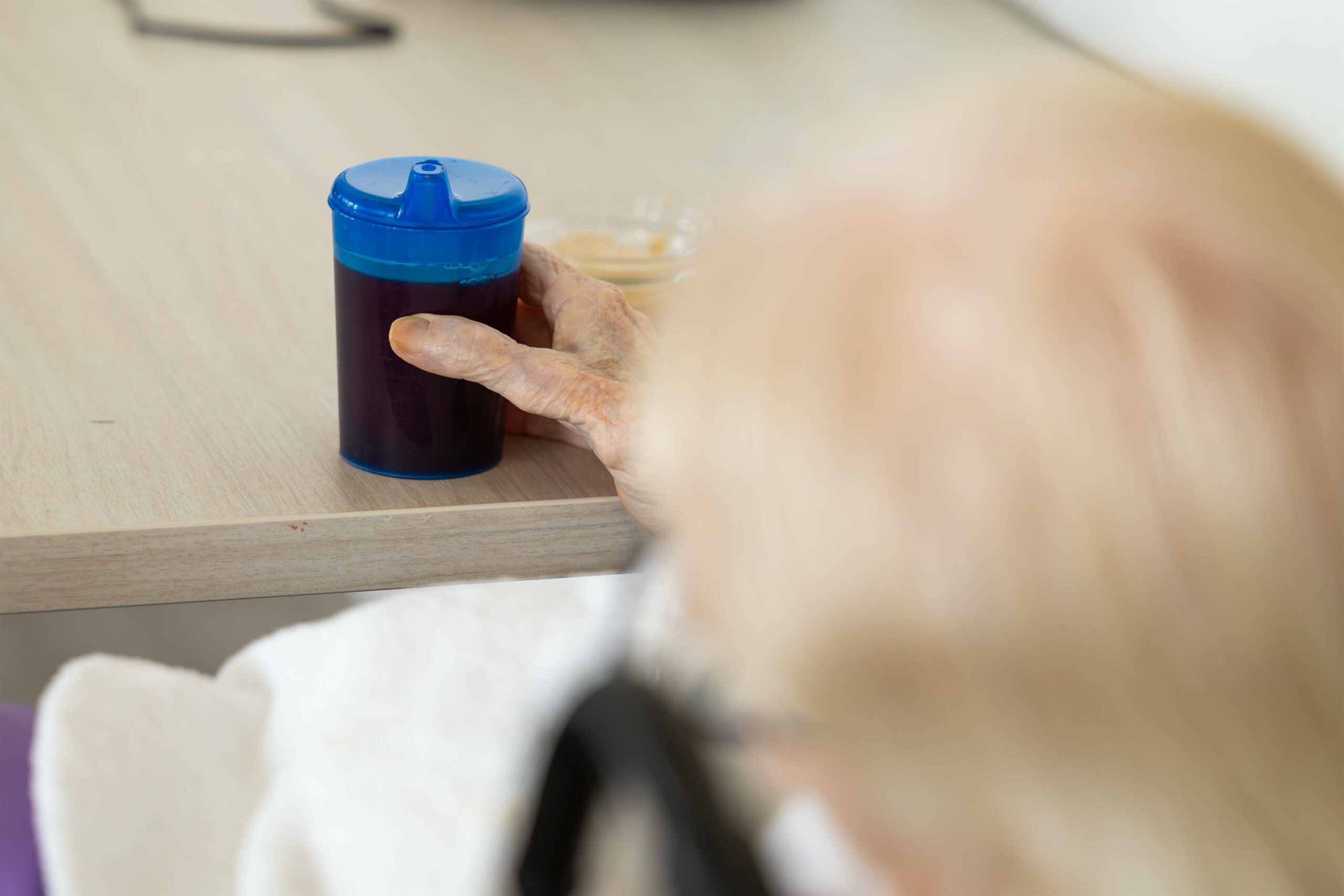 Eine alte Frau sitzt mit einer Schnabeltasse in der Hand an einem Tisch. (Symbolfoto)