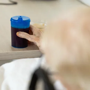 Eine alte Frau sitzt mit einer Schnabeltasse in der Hand an einem Tisch. (Symbolfoto)