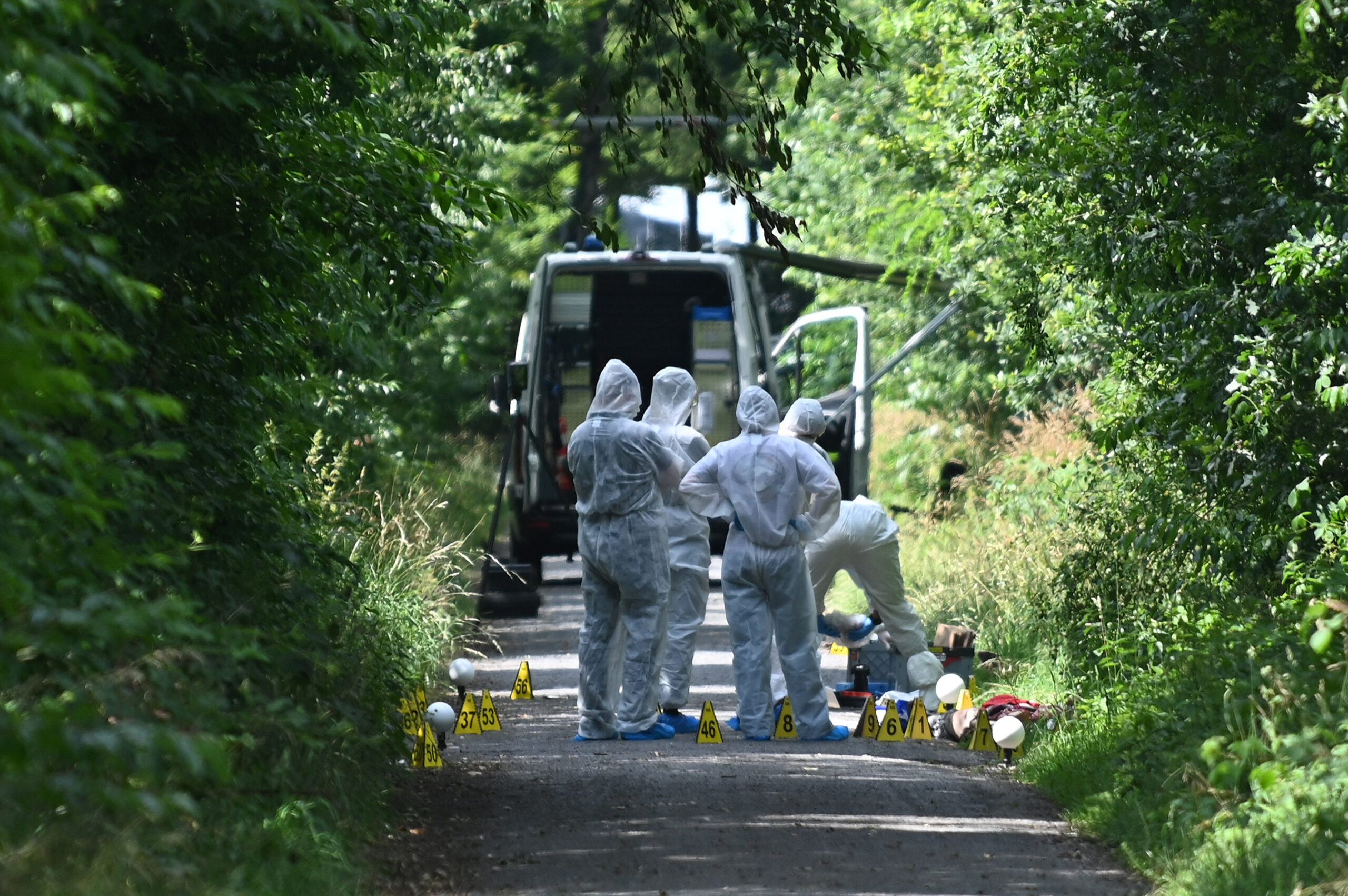 Ermittler in Schutzanzügen stehen auf einem Weg.