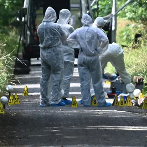 Ermittler in Schutzanzügen stehen auf einem Weg.