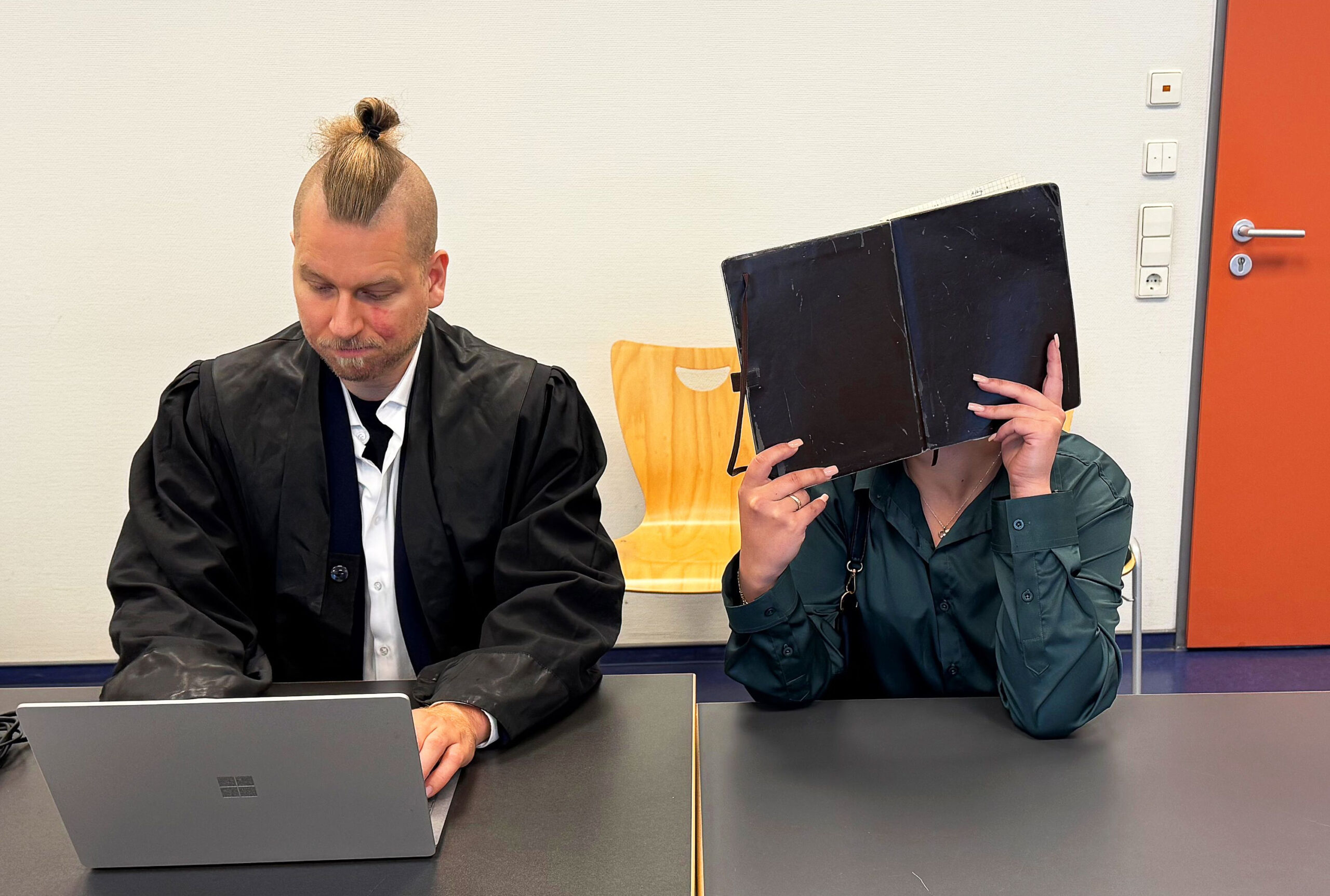 Die Angeklagte sitzt neben ihrem Verteidiger und verdeckt ihr Gesicht.