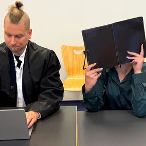Die Angeklagte sitzt neben ihrem Verteidiger und verdeckt ihr Gesicht.