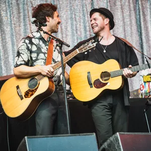 Beide mit Gitarren, sie lachen und umarmen sich
