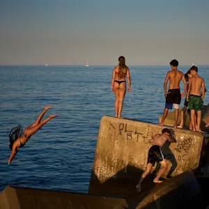 Junge Schwimmer springen an einem heißen Tag von einem Wellenbrecher ins Wasser.