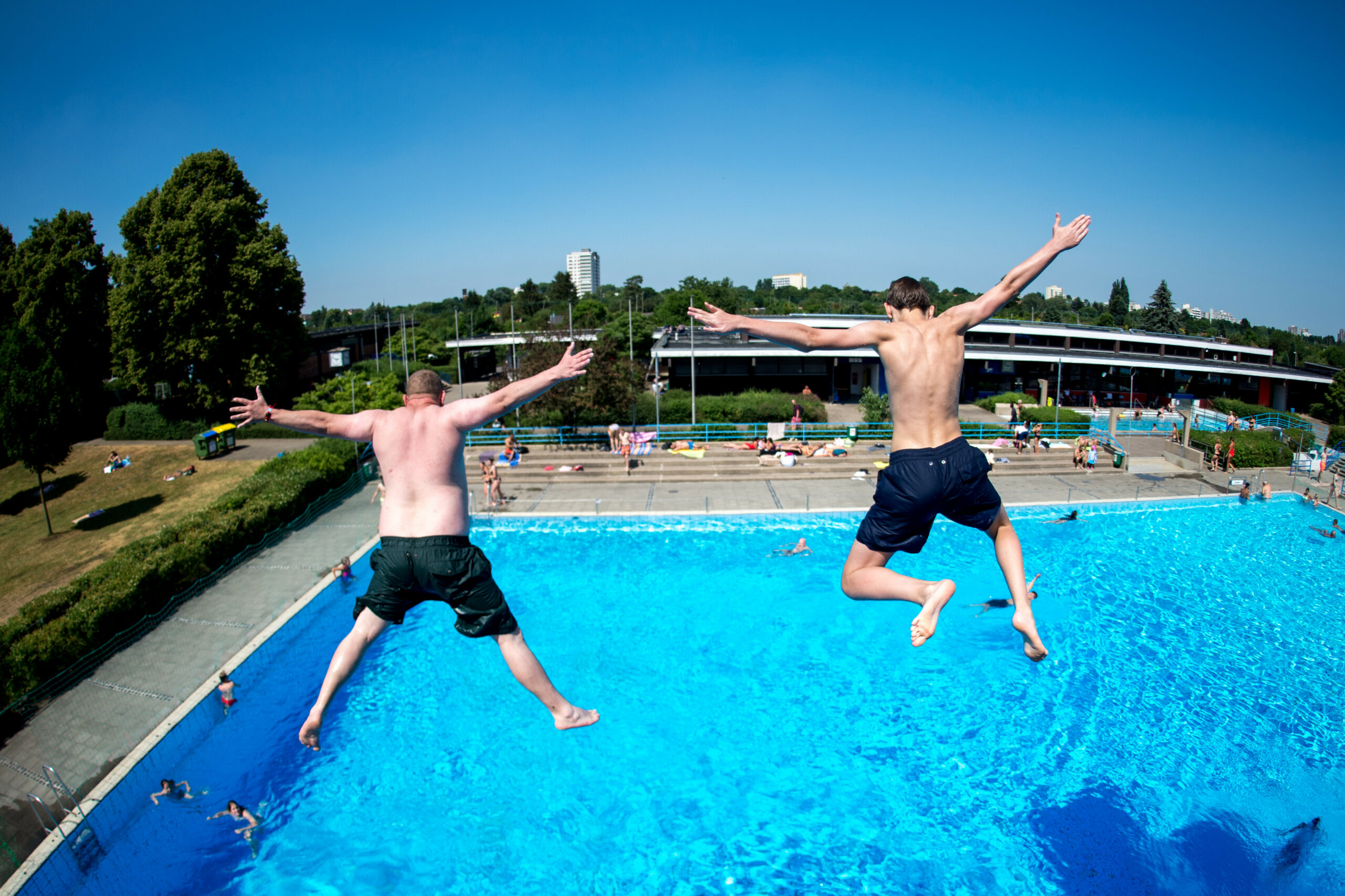 Zwei junge Männer springen von einem Sprungturm in ein Schwimmbecken im Lister Freibad