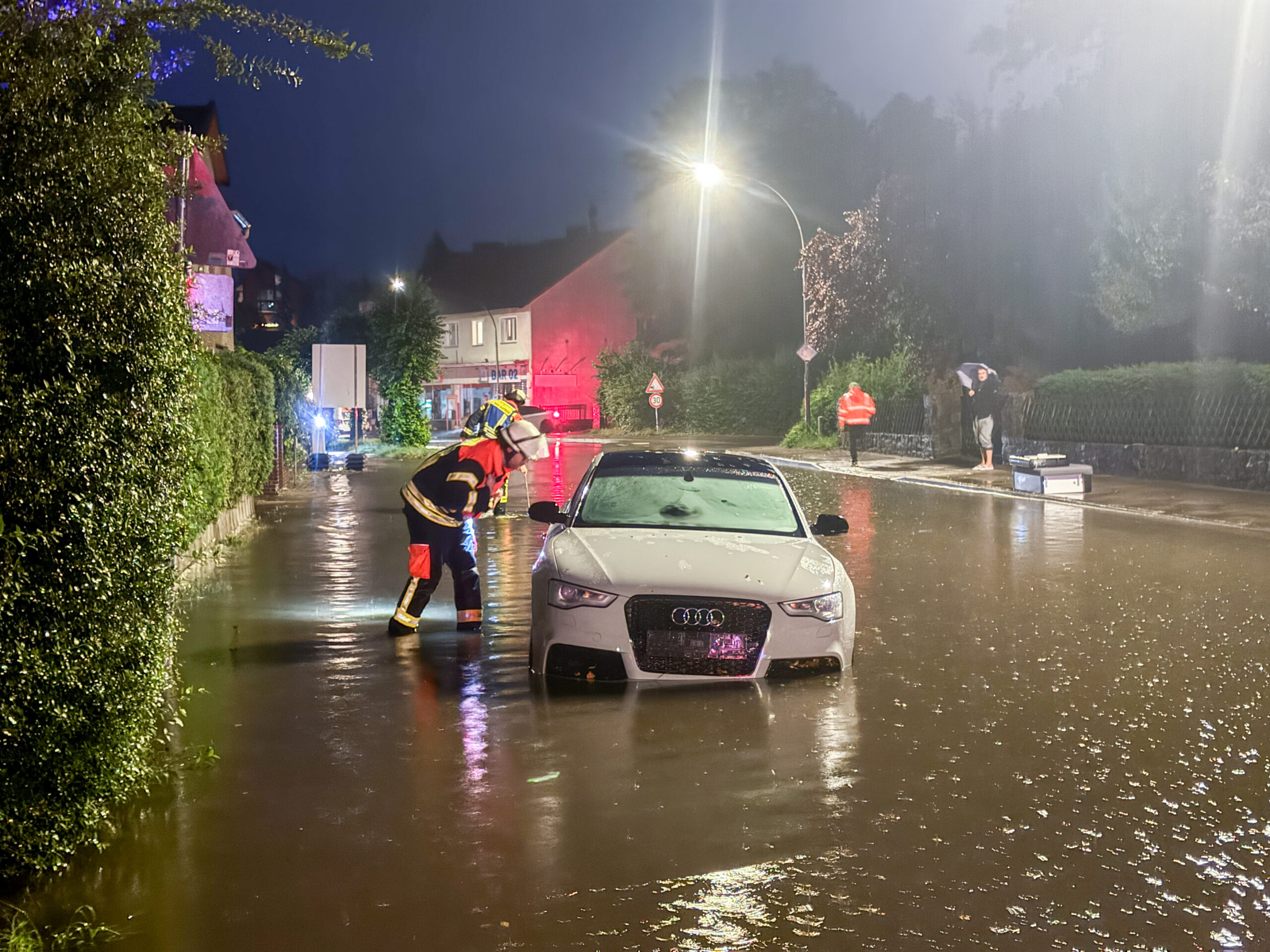 Ein Feuerwehrmann kontrolliert ein Fahrzeug, dessen Insassen durch den Starkregen in Not geraten sind.