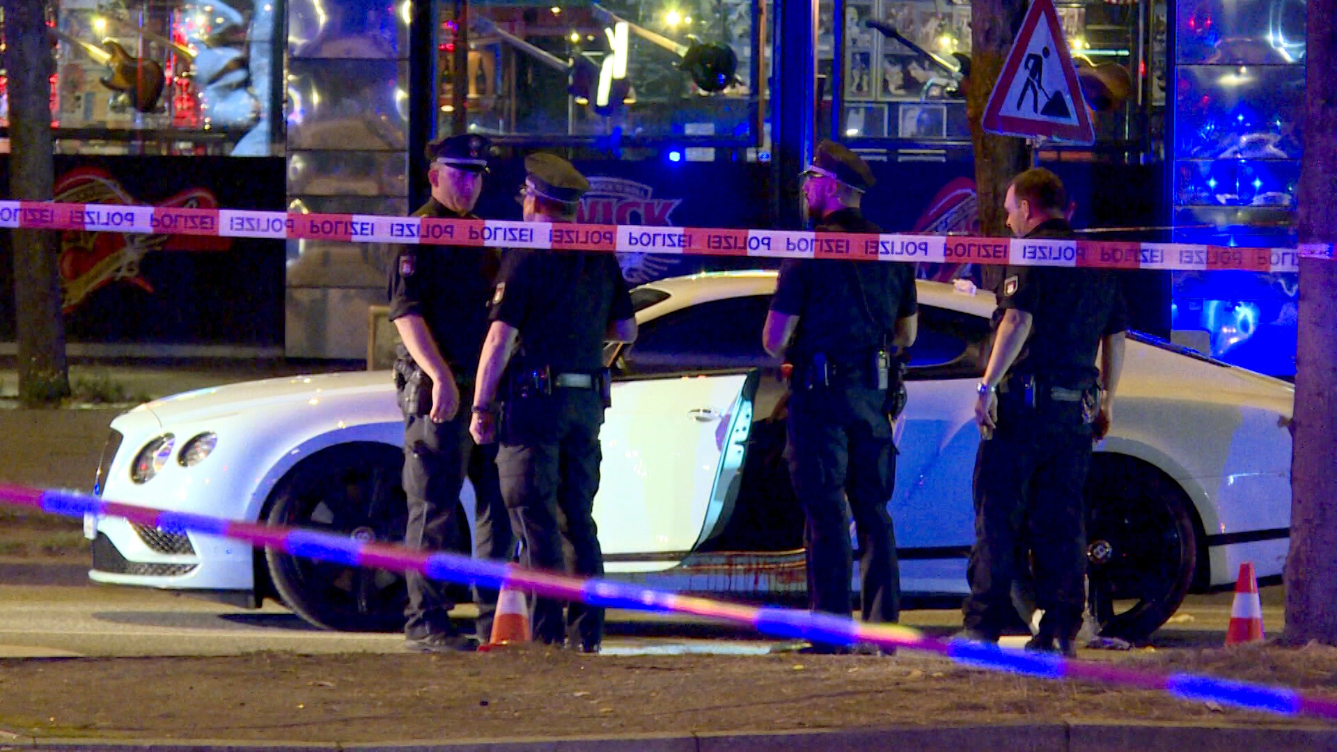Polizisten stehen hinter Absperrband um ein weißes Auto herum.