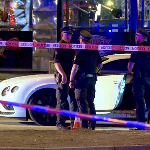 Polizisten stehen hinter Absperrband um ein weißes Auto herum.