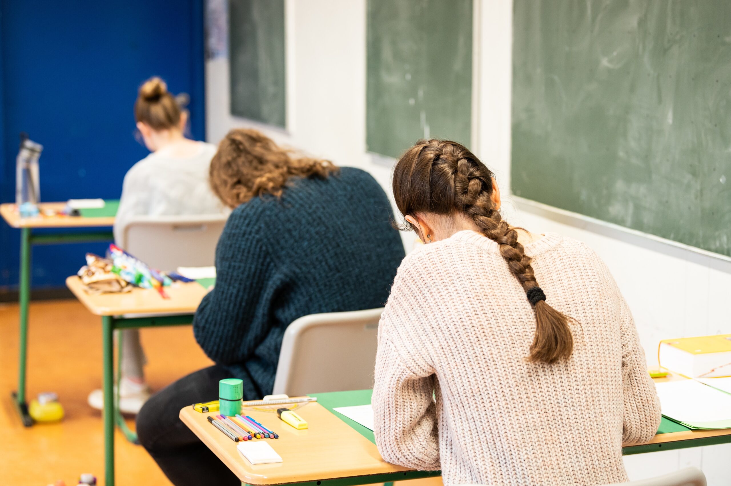 Schüler:innen sitzen in einem Klassenzimmer und schreiben das Biologie-Abitur.
