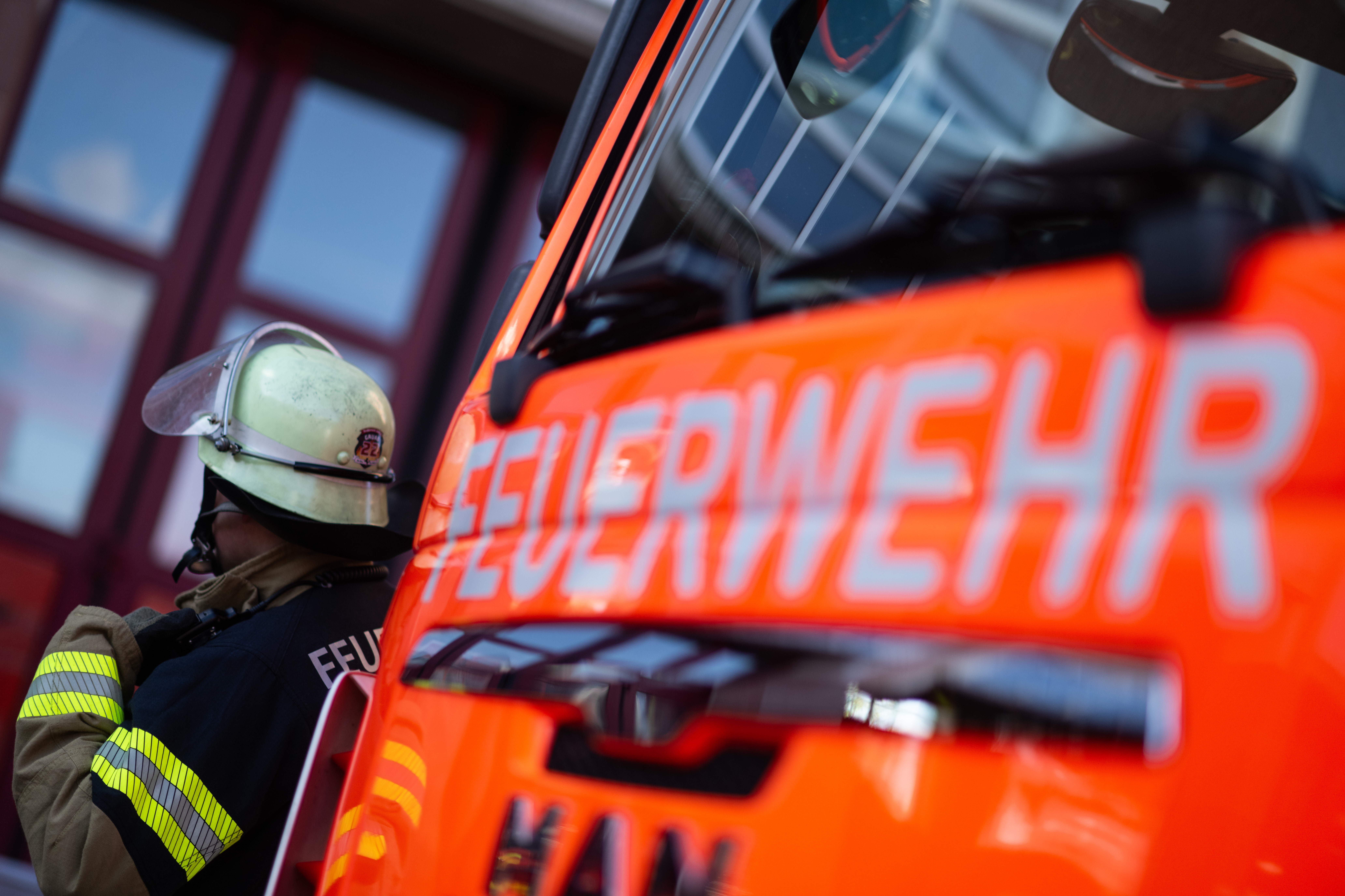 Hinter einem Feuerwehrauto steht ein Feuerwehrmann.