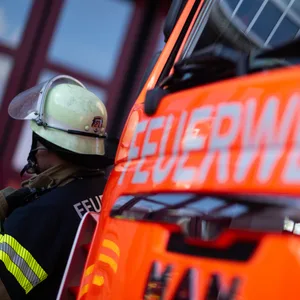 Hinter einem Feuerwehrauto steht ein Feuerwehrmann.