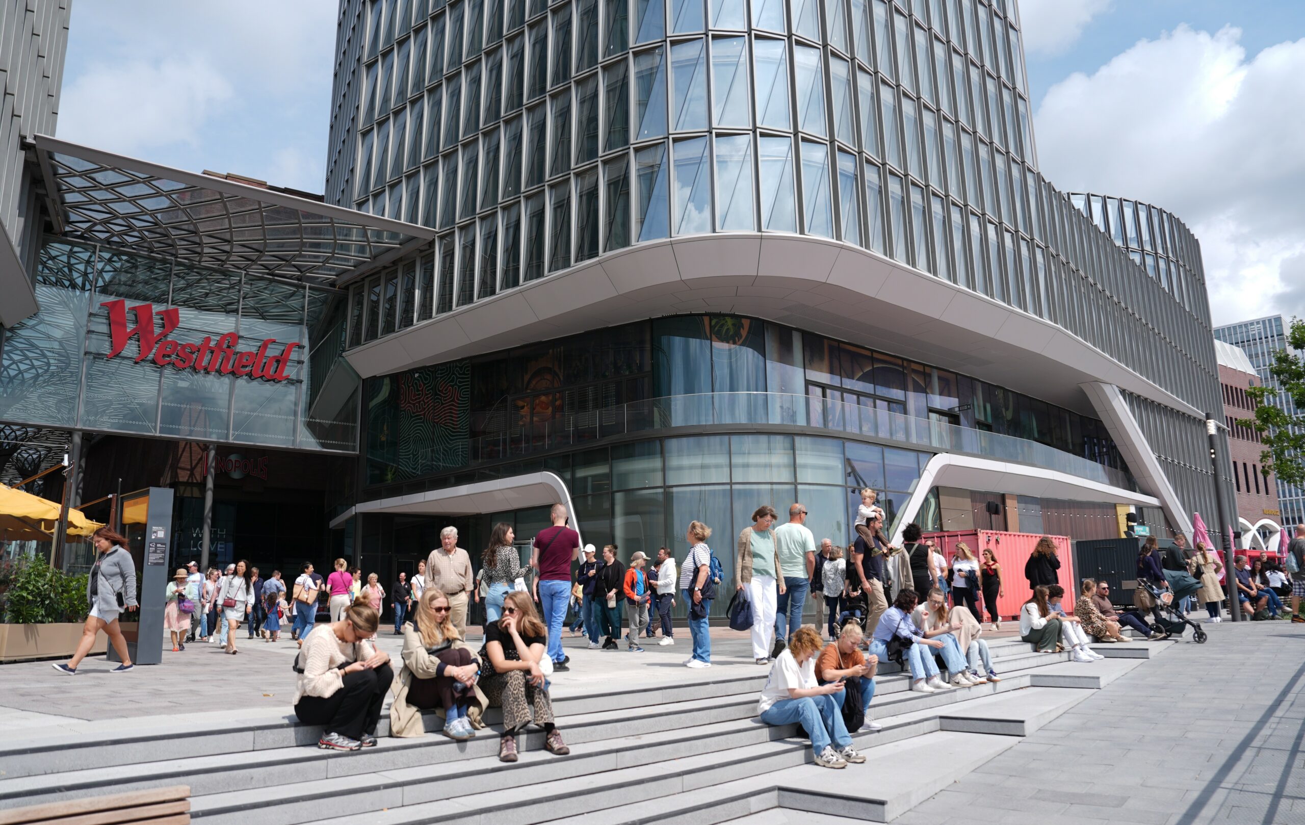 Besucherinnen und Besucher genießen am verkaufsoffene Sonntag auf dem Vorplatz des Einkaufscenters Westfield Hamburg-Überseequartier das gastronomische Angebot und das sonnige Wetter.