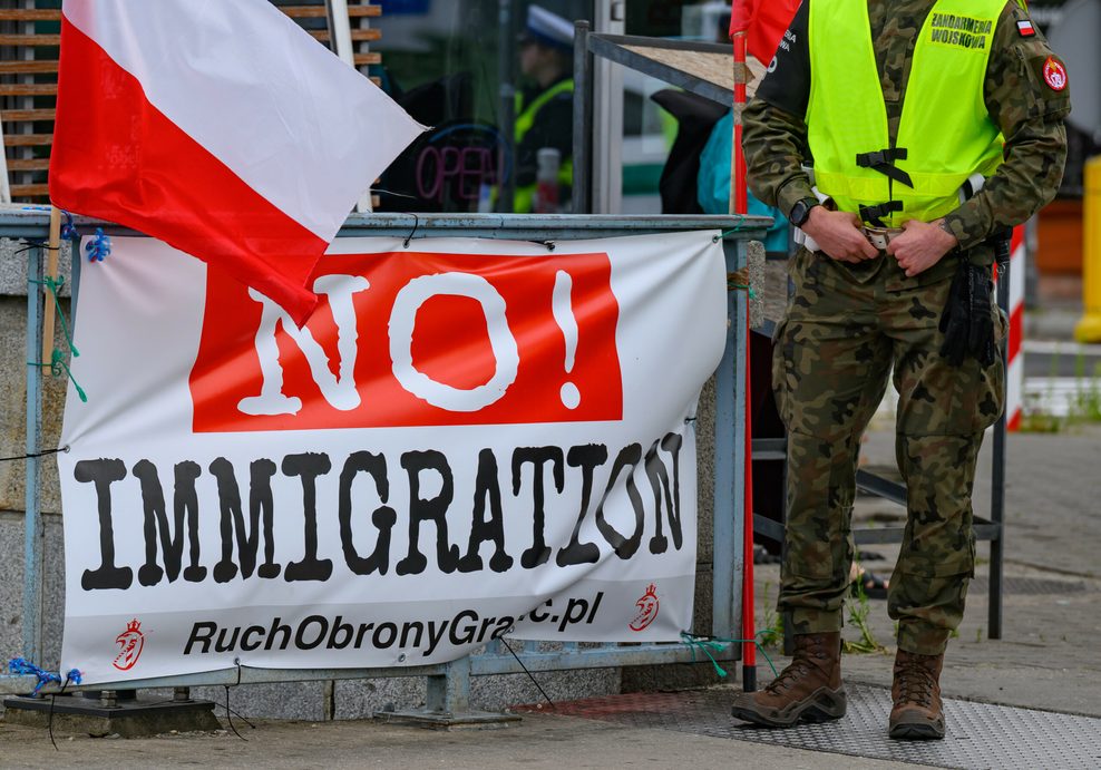 Ein polnischer Militärpolizist steht neben einem Transparent mit der Aufschrift „No! Immigration“