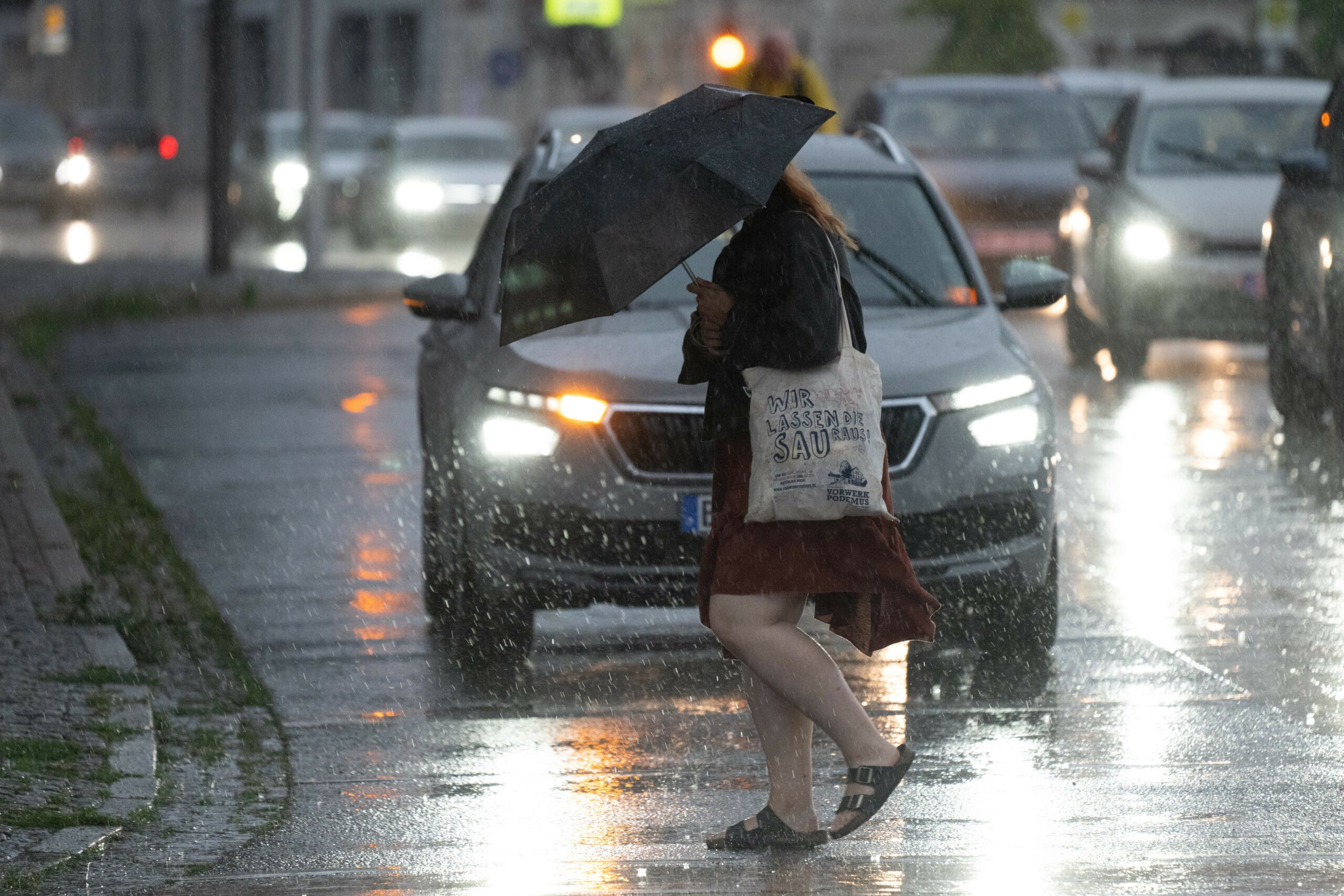 Eine Frau läuft mit einem Regenschirm über eine Straße