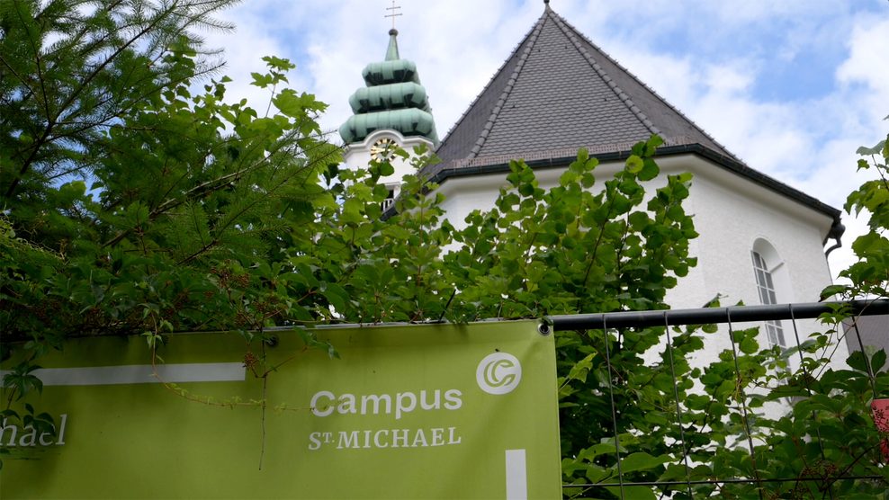 Das katholische Studienseminar St. Michael. Ein weißes Gebäude mit spitzem Dach steht hinter einer Hecke. Davor hängt ein grünes Schild mit der Aufschrift: „Campus St. Michael“.