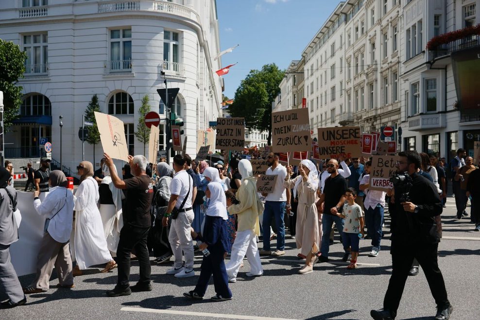 Demonstranten ziehen mit Pappschildern am Hotel Atlantic vorbei.