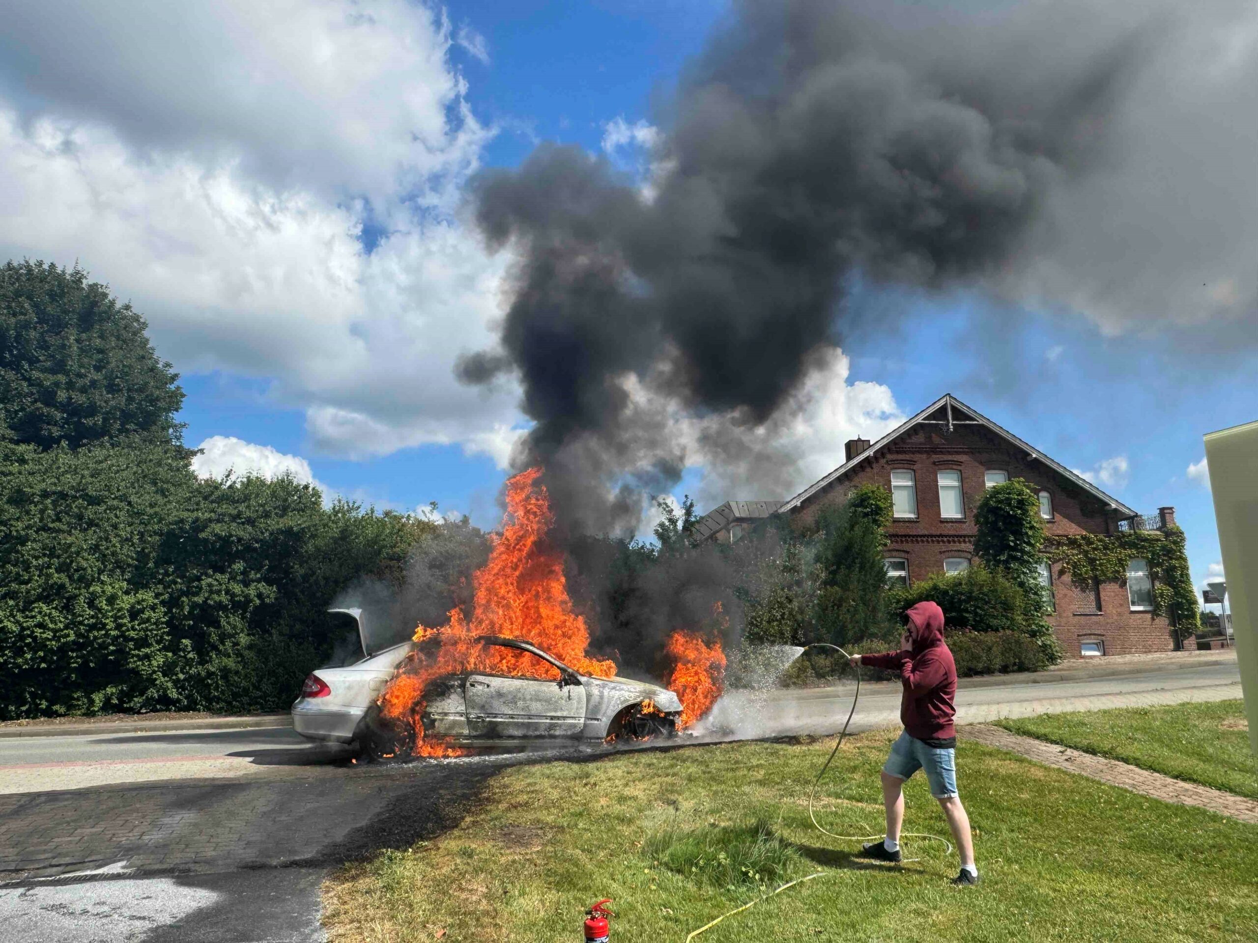 Ein Anwohner versucht, das brennende Auto in Guderhandviertel mit einem Gartenschlauch zu löschen.
