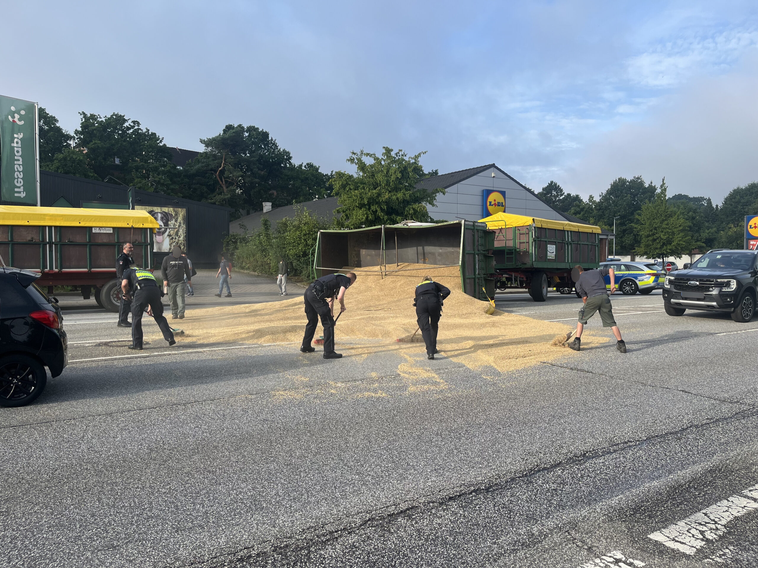 Polizisten schaufeln das Getreide von der Fahrbahn.