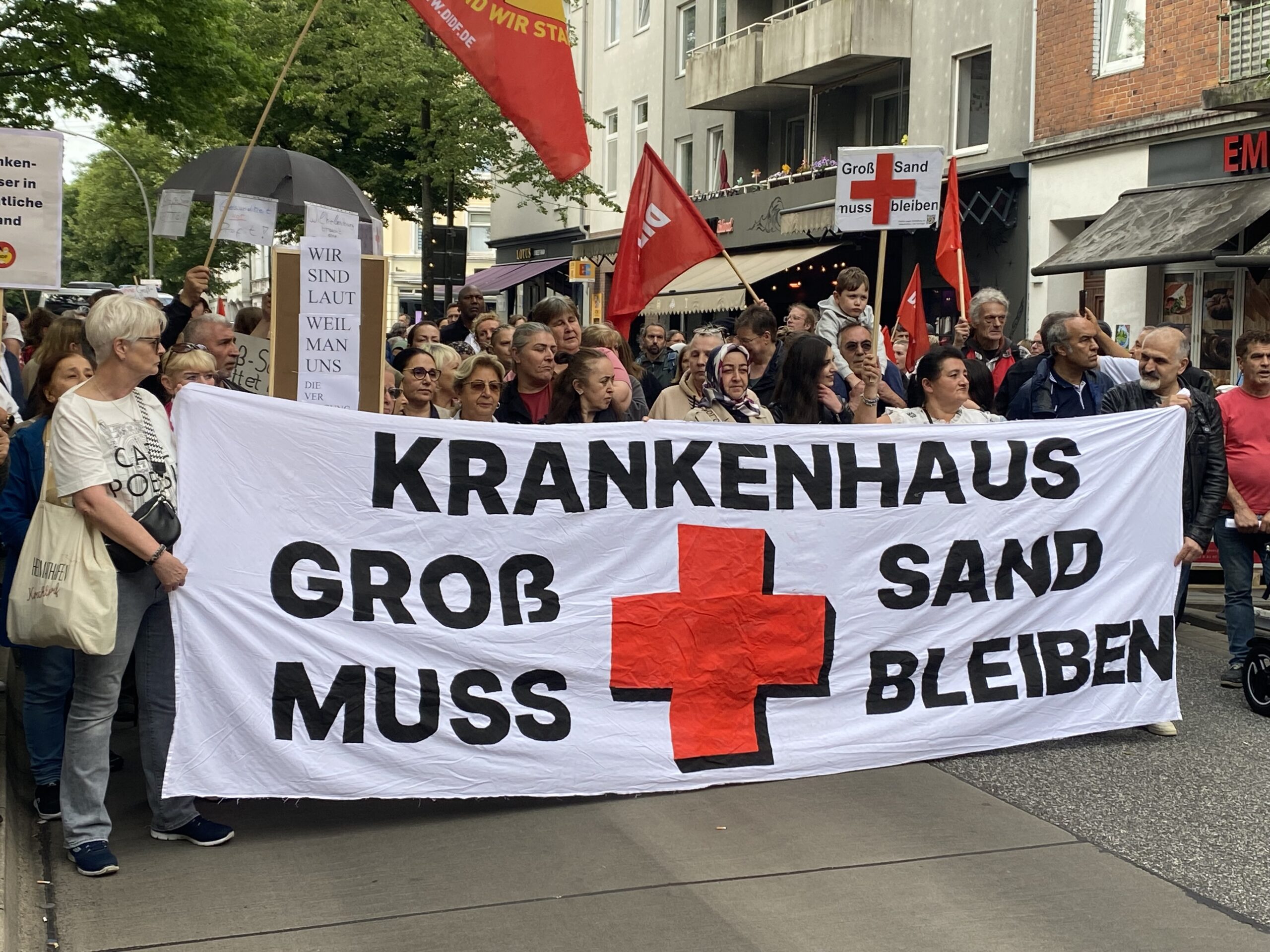 Demonstranten tragen ein Banner mit der Aufschrift: „Krankenhaus Groß-Sand muss bleiben“