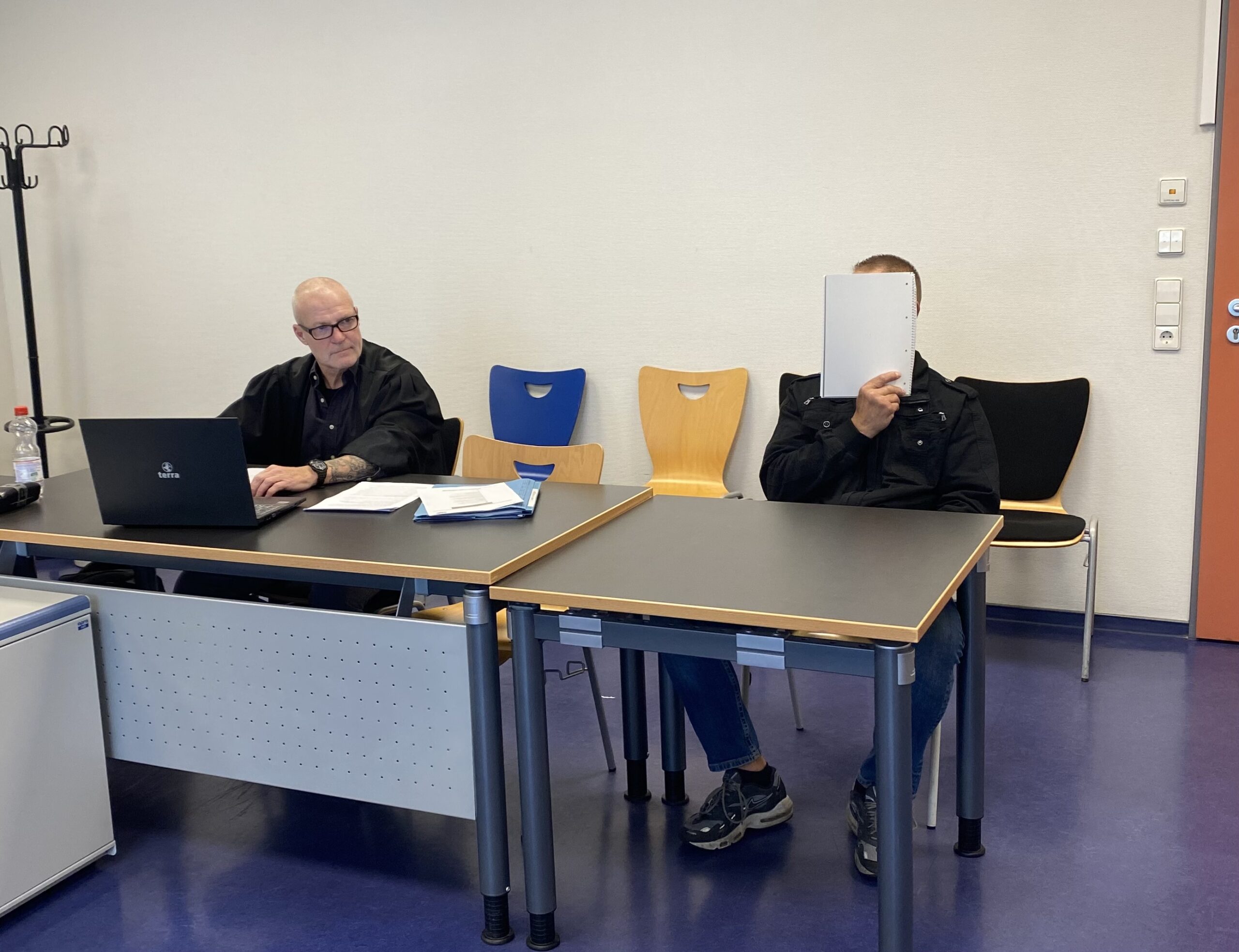 Der Angeklagte Michael L. sitzt neben seinem Verteidiger. L. hält sich ein Papier vor das Gesicht.