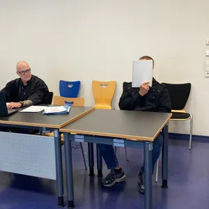 Der Angeklagte Michael L. sitzt neben seinem Verteidiger. L. hält sich ein Papier vor das Gesicht.