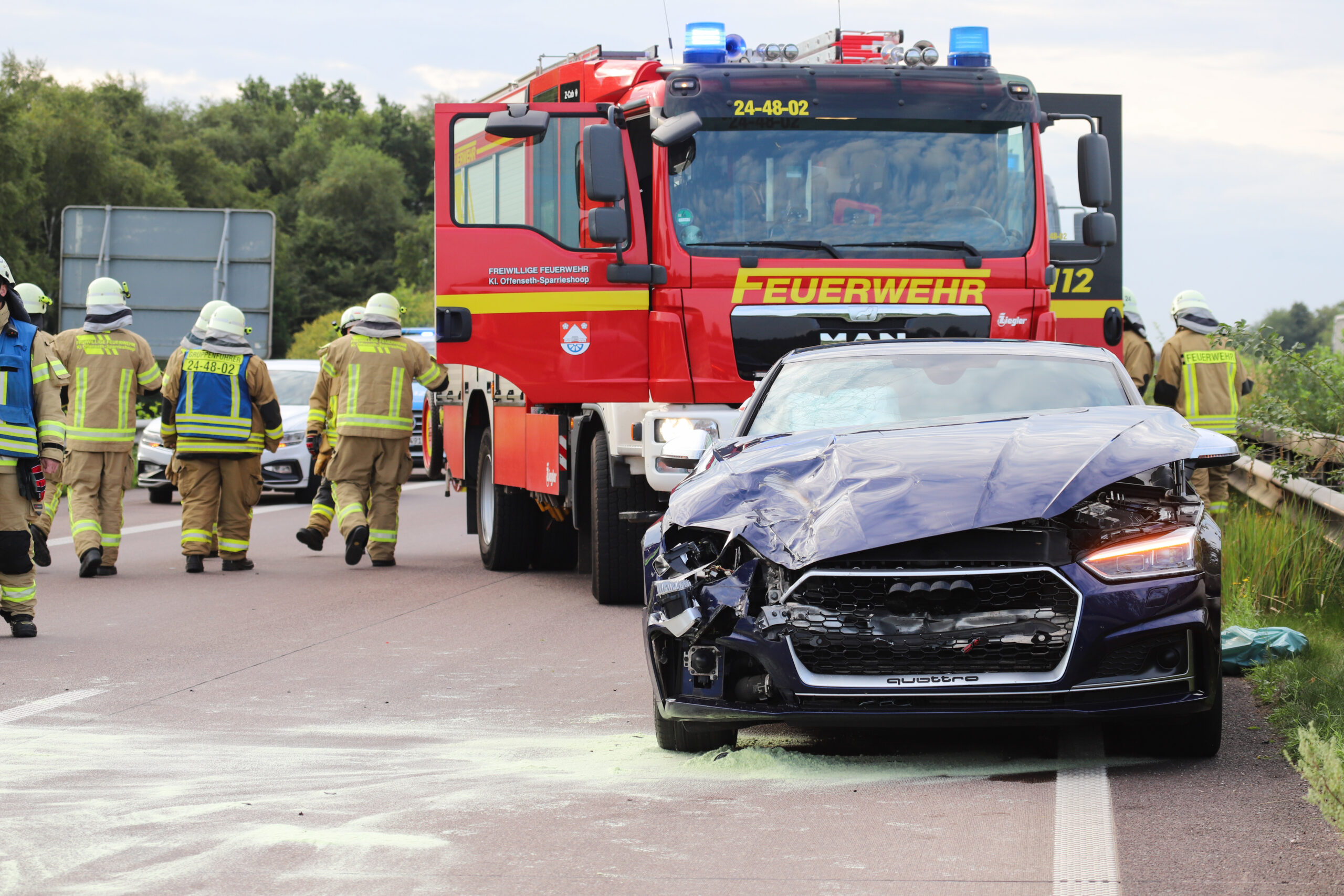 Ein zerbeulter schwarzer Audi steht vor einem Einsatzwagen der Feuerwehr.